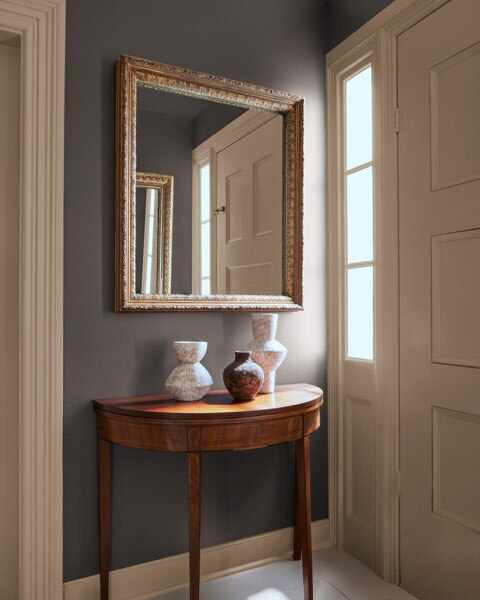 A hallway with semi-circular table decorated with vases. The walls and ceilings are colour drenched in Silhouette AF-655 with contrasting Sherwood Tan 1054 on the woodwork and doors.
